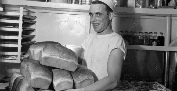 Photo d’un boulanger dans la cuisine du NCSM Haida avec de nombreuses miches de pain